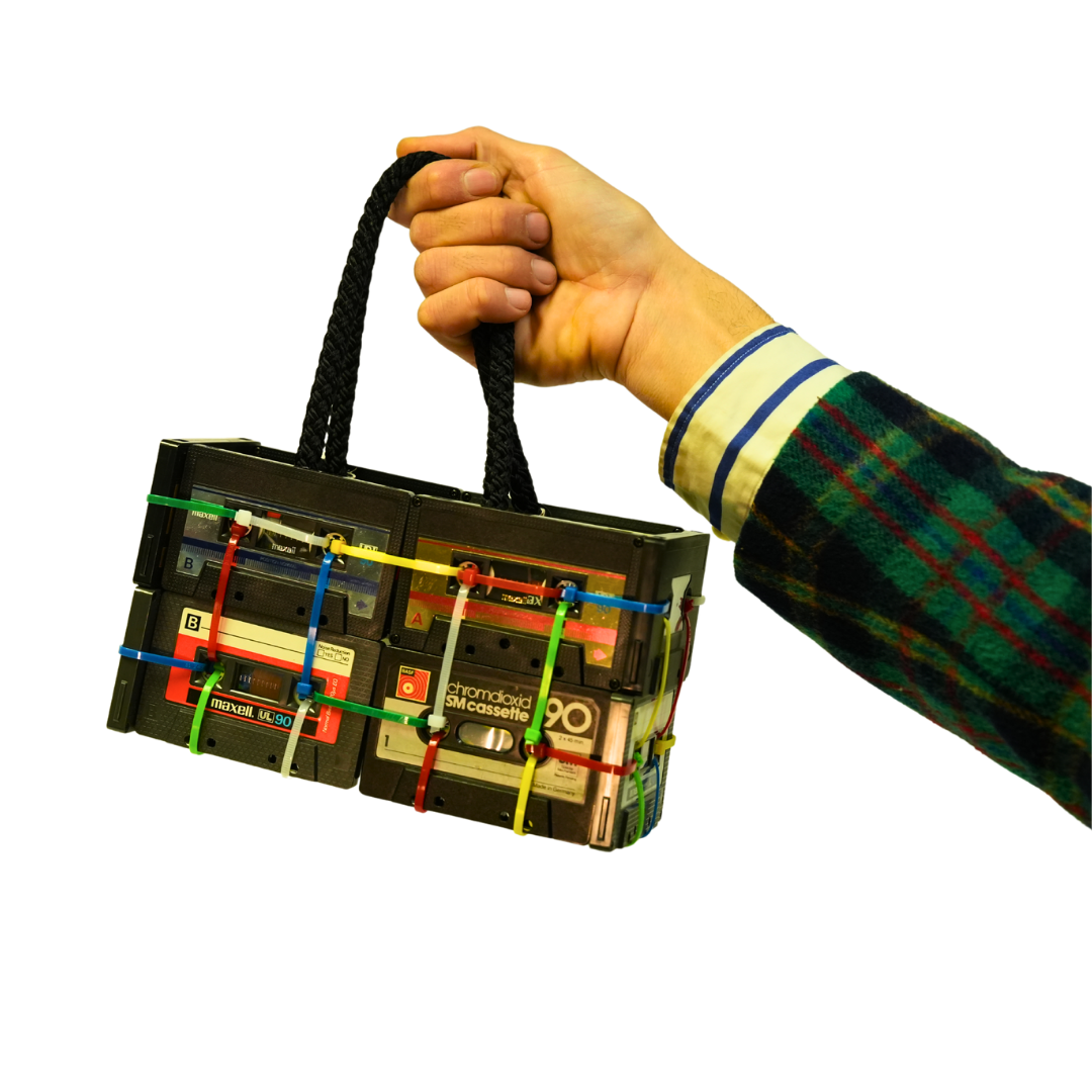 Hand holding a bag made from recycled cassette tapes on a white background