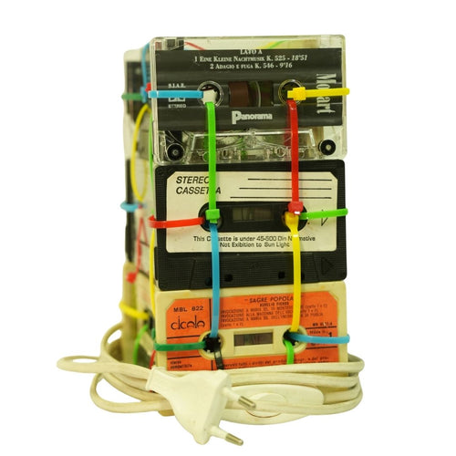 Stack of vintage audio cassettes with colorful bands and a power cord on a white background