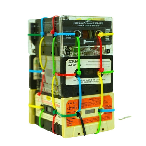 Stack of vintage cassette tapes with colorful strings on a white background