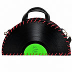 A novelty handbag designed to look like a vinyl record, featuring a black body with red faux-stitch details around the edge and a bright green center label with handwritten text that reads 'Sorry I missed a stop.'.