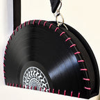 A black vinyl record purse with pink contrast stitching along the rim, a silver metal clasp, and a black hanging strap, shown against a plain light background.