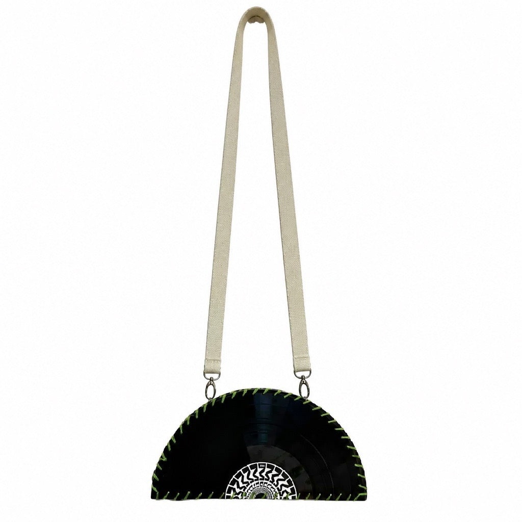 A black vinyl record half-moon shoulder bag with a cream-colored fabric strap and a white geometric pattern on the center, shown against a plain white background.