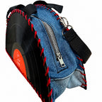 A denim crossbody bag styled like a vinyl record, featuring a blue denim body, black vinyl-style side, red stitching, black straps, and a silver zipper.