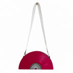 A bright pink vinyl record style shoulder bag with a white strap and a black and white circular graphic at the bottom center, shown against a plain white background.