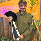Man holding a black hat with a white strap against a colorful outdoor background. francesca farfa black fan
