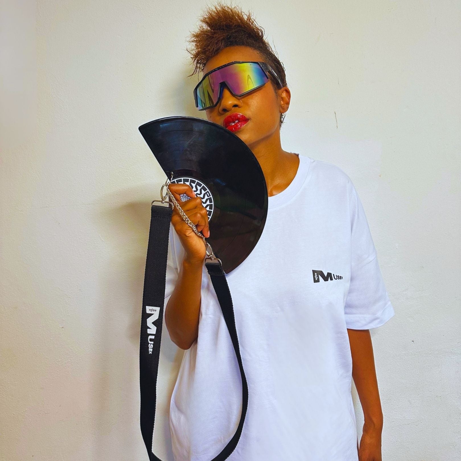 Person holding a black fan with a strap, wearing a white t-shirt and colorful sunglasses against a plain background. francesca farfa black fan