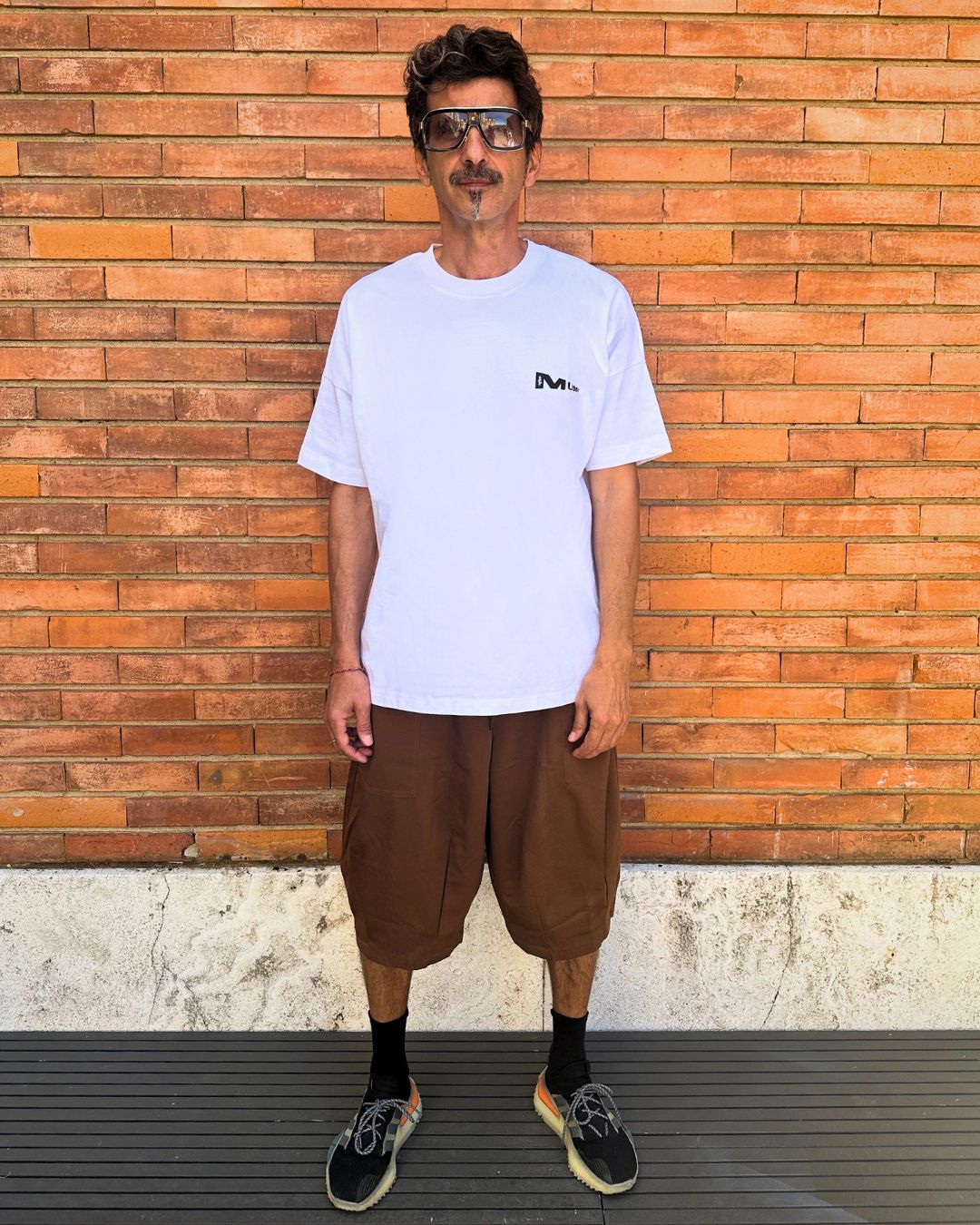 francesca farfa t shirt. Man wearing a white t-shirt and brown shorts standing against a wooden wall.