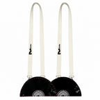Two black faux-fur shoulder bags with long off-white straps, shown side by side on a plain white background. Each bag features a circular silver-toned metal emblem on the front and a black logo printed on the strap.