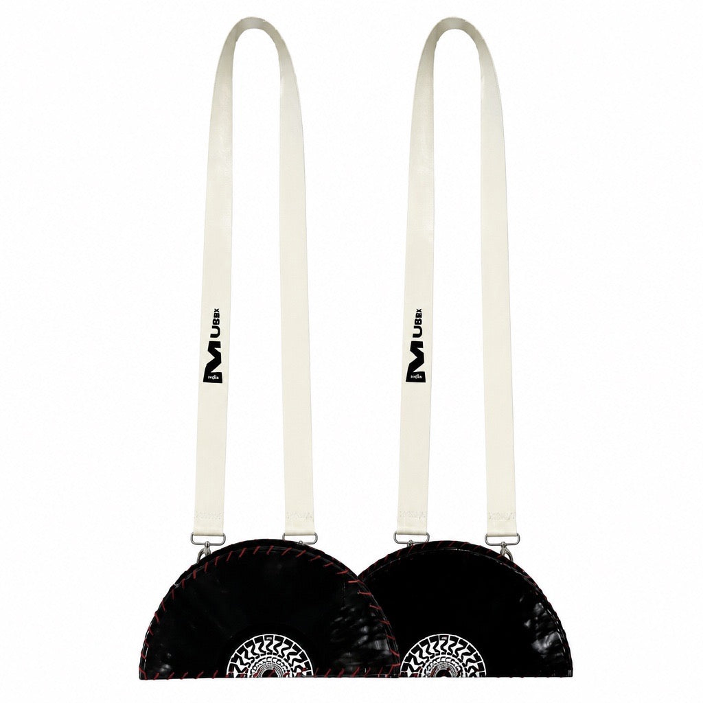 Two black faux-fur shoulder bags with long off-white straps, shown side by side on a plain white background. Each bag features a circular silver-toned metal emblem on the front and a black logo printed on the strap.