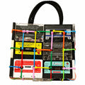 A novelty handbag designed to look like a clear plastic cassette-tape rack with a black braided top handle. The bag features multiple vintage cassette tapes in clear plastic, colorful plastic zip ties in green, pink, yellow, and blue, and labels from artists like Tabu and Daft Punk.