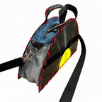 A handmade shoulder bag made from scrap materials, featuring a black 3D-printed side panel, a blue denim fabric top, a gray denim fabric front, red faux-stitch stitching, and a bright yellow circular patch. It has a black webbed strap and a metal clasp.
