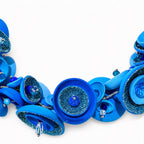 A vibrant blue handmade necklace featuring layered fabric rosettes, glittery blue textured centers, and small clear crystal beads, displayed on a clean white background. Silvia Tolomei best handmade jewelry in Tuscany. Tuscany jewelry. Tuscan jewelry. Populonia best store to visit. Things to do in populonia. 