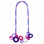 A colorful braided rope necklace with a gradient of purple and pink, featuring a cluster of crocheted rings in purple, pink, and white at the bottom, shown against a plain white background. Silvia Tolomei best handmade jewelry in Tuscany. Tuscany jewelry. Tuscan jewelry. Populonia best store to visit. Things to do in populonia. 