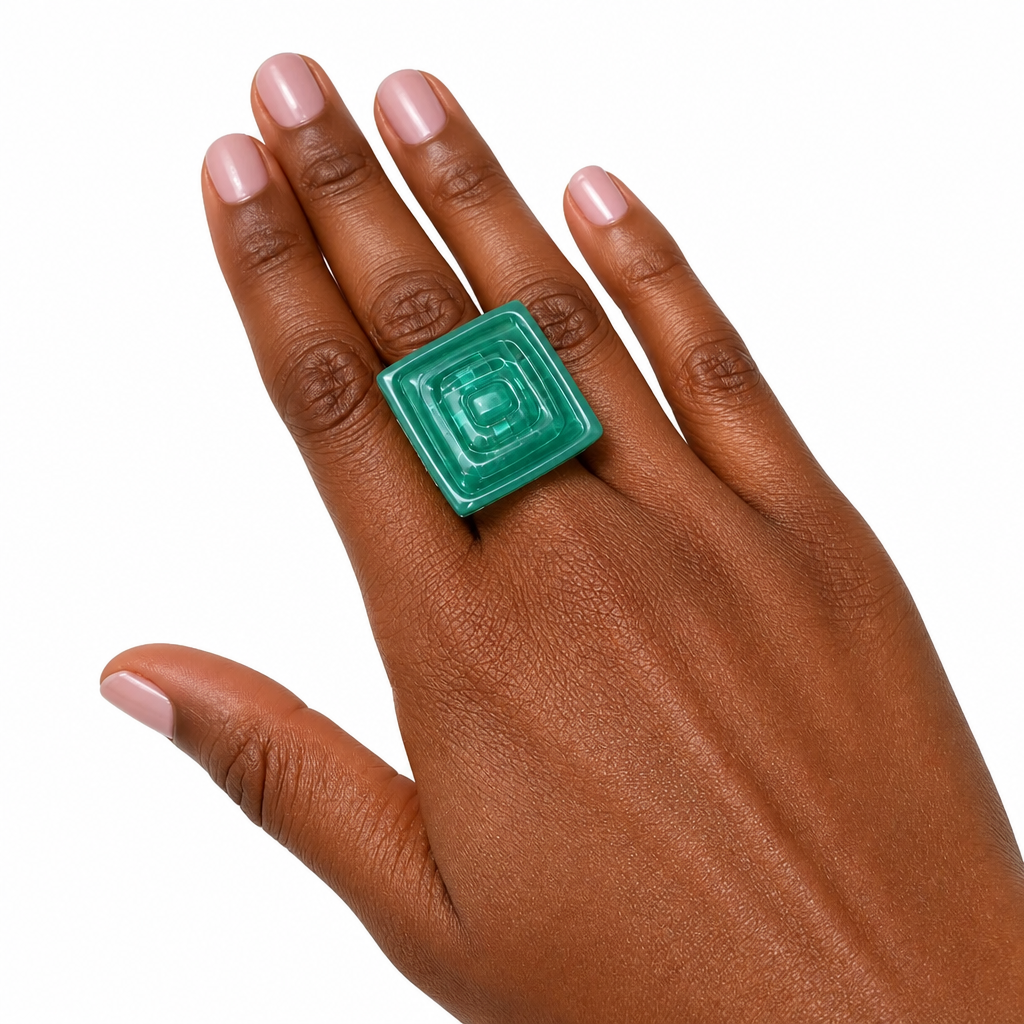 A close-up of a hand wearing a chunky, square-shaped green ring with a concentric square design, set against a plain white background. Silvia Tolomei best handmade jewelry in Tuscany. Tuscany jewelry. Tuscan jewelry. Populonia best store to visit. Things to do in populonia. 
