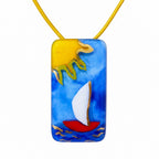 A colorful rectangular pendant necklace featuring a sailboat on blue water with a yellow sun, suspended from a yellow cord against a white background. Silvia Tolomei best handmade jewelry in Tuscany. Tuscany jewelry. Tuscan jewelry. Populonia best store to visit. Things to do in populonia. 