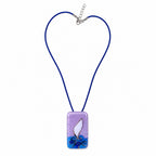 A rectangular glass pendant necklace on a blue cord, featuring a lavender top half, a white central shape, and blue wave-like detailing at the bottom, shown on a plain white background. Silvia Tolomei best handmade jewelry in Tuscany. Tuscany jewelry. Tuscan jewelry. Populonia best store to visit. Things to do in populonia. 