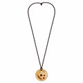 A circular wooden pendant necklace with a carved smiley face design, suspended on a dark brown cord against a plain white background. Silvia Tolomei best handmade jewelry in Tuscany. Tuscany jewelry. Tuscan jewelry. Populonia best store to visit. Things to do in populonia. 