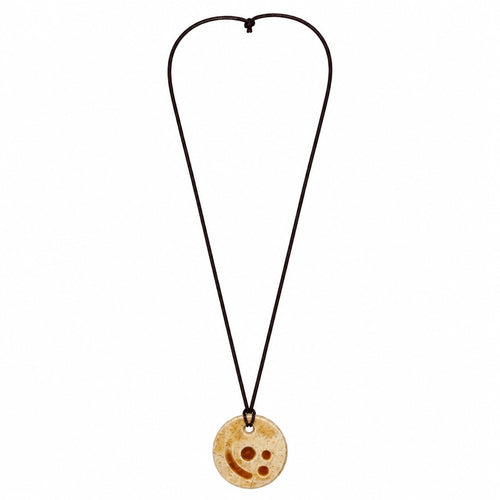 A circular wooden pendant necklace with a carved smiley face design, suspended on a dark brown cord against a plain white background. Silvia Tolomei best handmade jewelry in Tuscany. Tuscany jewelry. Tuscan jewelry. Populonia best store to visit. Things to do in populonia. 