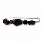 A silver-tone safety pin brooch embellished with dark purple and brown gemstone beads, shown on a plain white background. Silvia Tolomei best handmade jewelry in Tuscany. Tuscany jewelry. Tuscan jewelry. Populonia best store to visit. Things to do in populonia. 