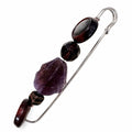 A silver-toned safety pin styled as a beaded brooch, featuring a large purple amethyst stone, a faceted dark red stone, and smaller dark brown and black beads, set against a plain white background. Silvia Tolomei best handmade jewelry in Tuscany. Tuscany jewelry. Tuscan jewelry. Populonia best store to visit. Things to do in populonia. 