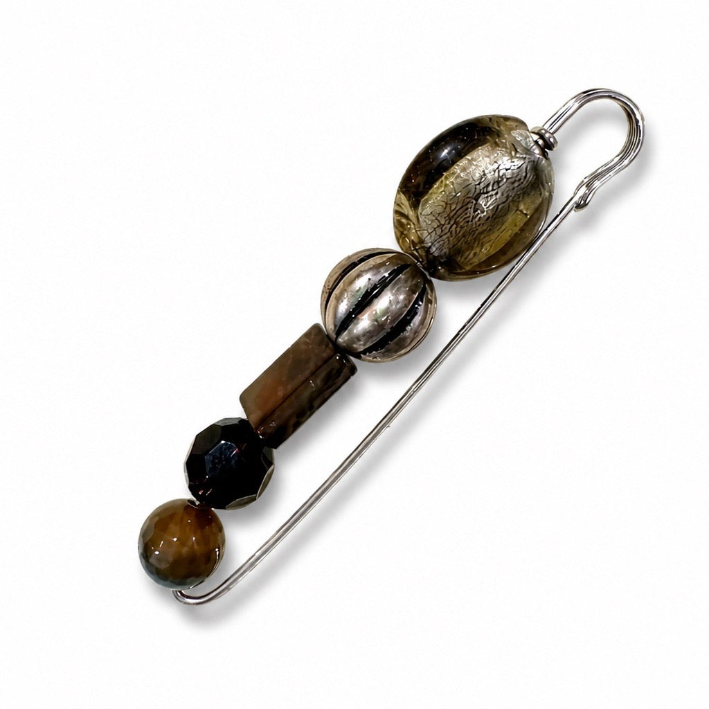 A silver safety pin styled as a beaded accessory with four decorative beads in brown, black, and metallic silver, set against a plain white background.