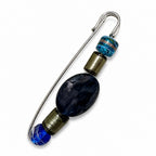 A silver safety pin styled as a beaded earring, featuring a large dark blue marbled bead, smaller blue beads, and metallic bronze-colored spacer rings, shown on a plain white background. Silvia Tolomei best handmade jewelry in Tuscany. Tuscany jewelry. Tuscan jewelry. Populonia best store to visit. Things to do in populonia. 
