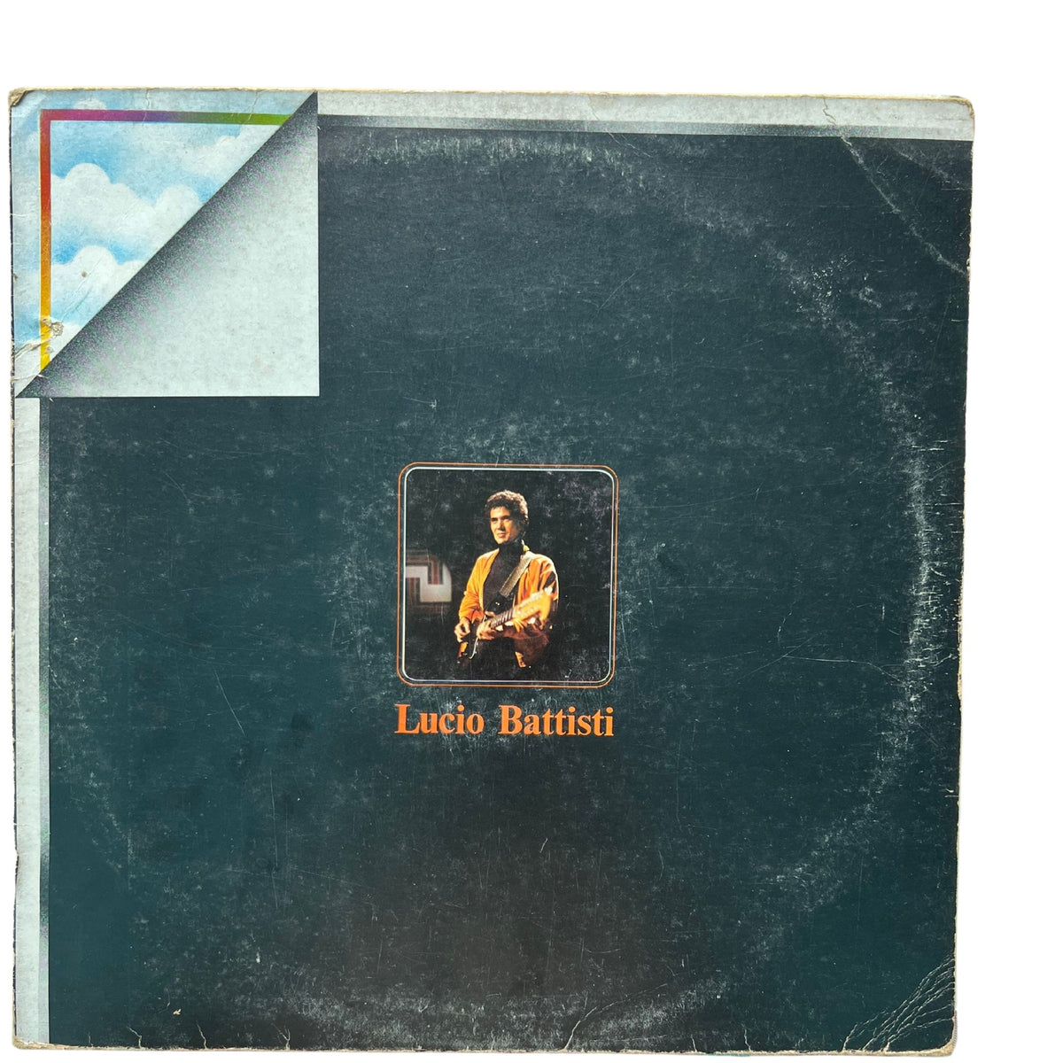 A vintage Lucio Battisti vinyl record album cover, likely a 12-inch LP, showing a dark teal-green textured background with a central portrait of the artist and orange text. The top-left corner is shown peeled back to reveal a light blue underside with a small rainbow-colored border detail.
