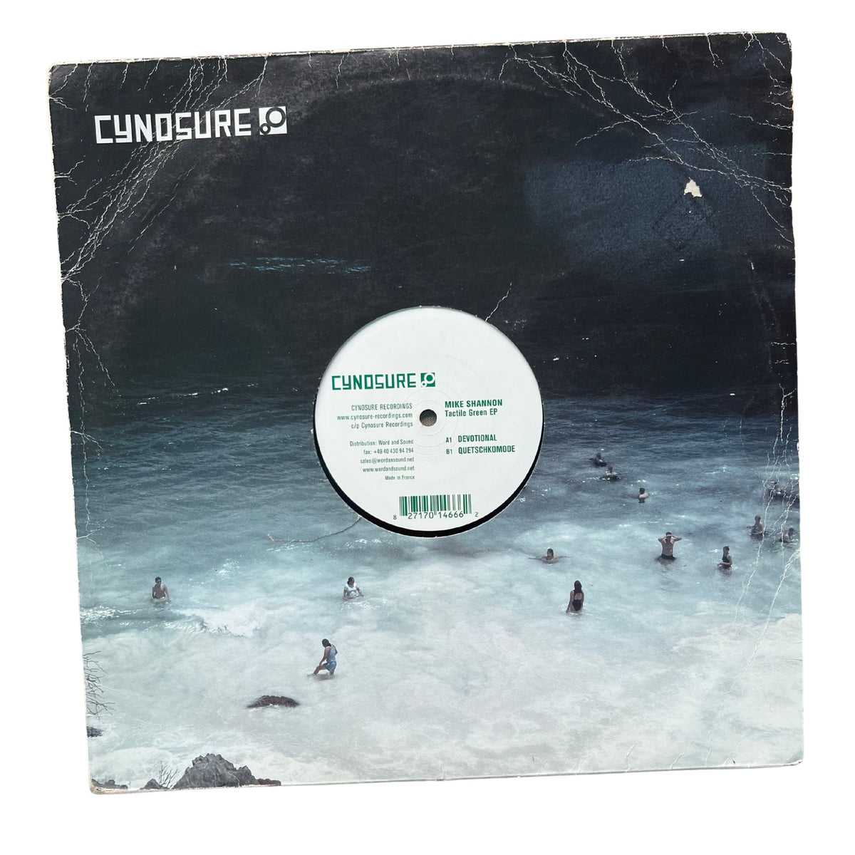 A vinyl record sleeve for Cynosure's 'Wave Scanner' LP, featuring a dark, moody ocean scene with surfers on the cover. The white center label of the vinyl is visible, and the record is photographed flat against a white background.