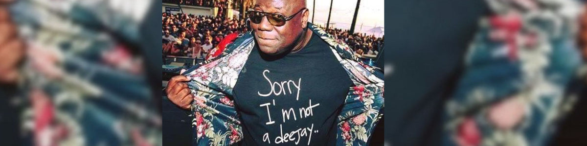 A man wearing a black graphic T-shirt with the text 'Sorry I'm not a decap' and a floral-patterned jacket, shown in a crowded outdoor setting.