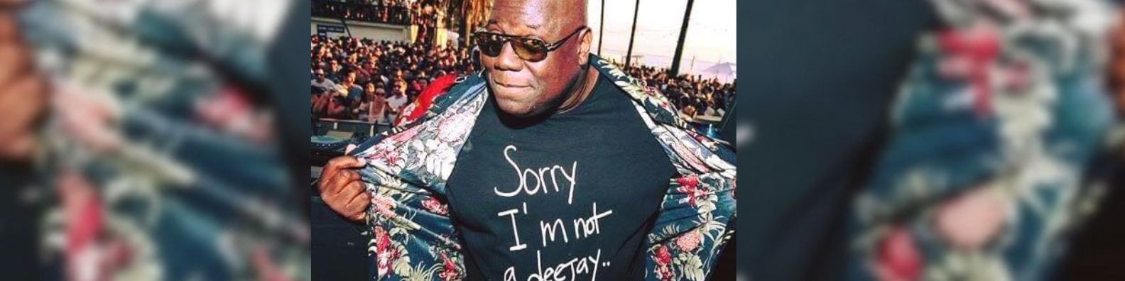 Person wearing a black t-shirt with text and a floral jacket in a crowd setting