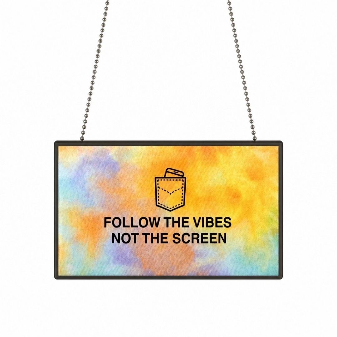 A rectangular hanging sign with a colorful watercolor-style background in yellow, orange, blue, and purple, featuring a small pocket graphic and the text 'FOLLOW THE VIBES NOT THE SCREEN' in black. Two metal ball chains extend upward against a plain white background.