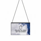 A rectangular hanging wall sign with a black ball chain, featuring a blue and white watercolor design and the text 'FOLLOW THE VIBES NOT THE SCREEN' with a small pocket graphic above it, shown on a plain white background.