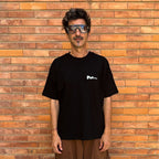 Man wearing a black t-shirt with a logo in front of a brick wall. Francesa Farfa black musek label t shirt