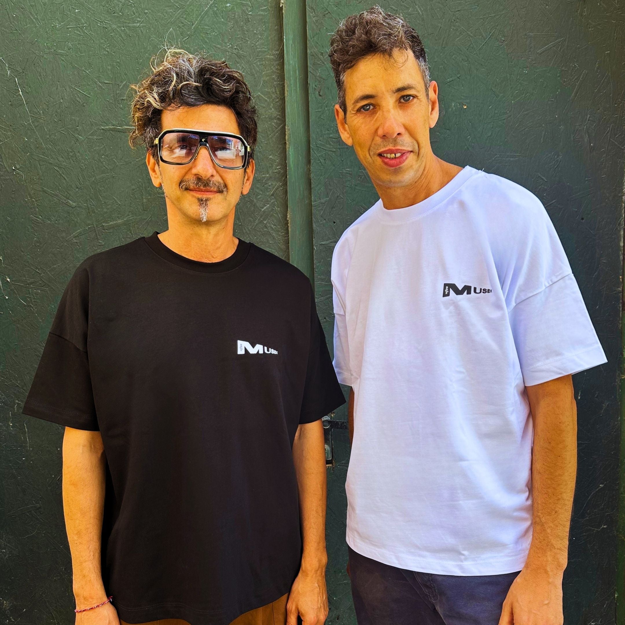 Two men wearing black and white t-shirts with a logo against a green wall. Man wearing a black t-shirt with a logo in front of a brick wall. Francesa Farfa black musek label t shirt