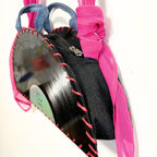 A handmade black fabric purse decorated with a vinyl record applique, pink sheer trim, and a bright pink ribbon handle, shown against a plain white background.